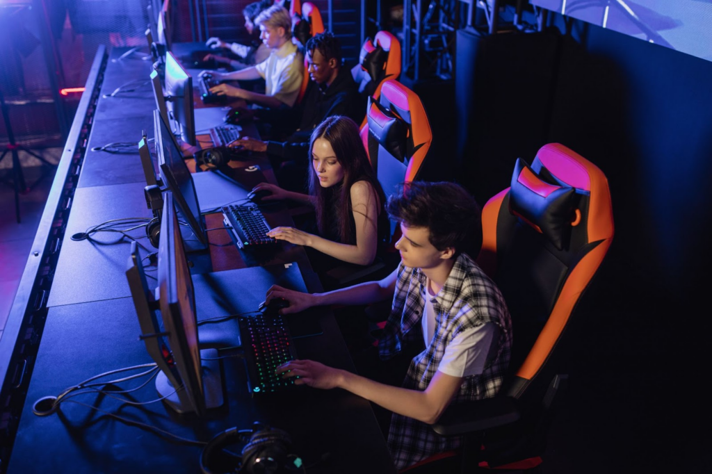 Group of 5 people sitting on gaming chairs facing computer screens