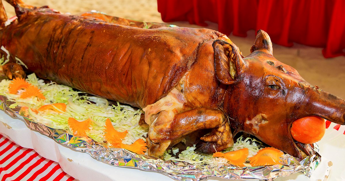 A whole roasted lechon, a famous Filipino dish, served on a festive table with garnishes and vegetables.