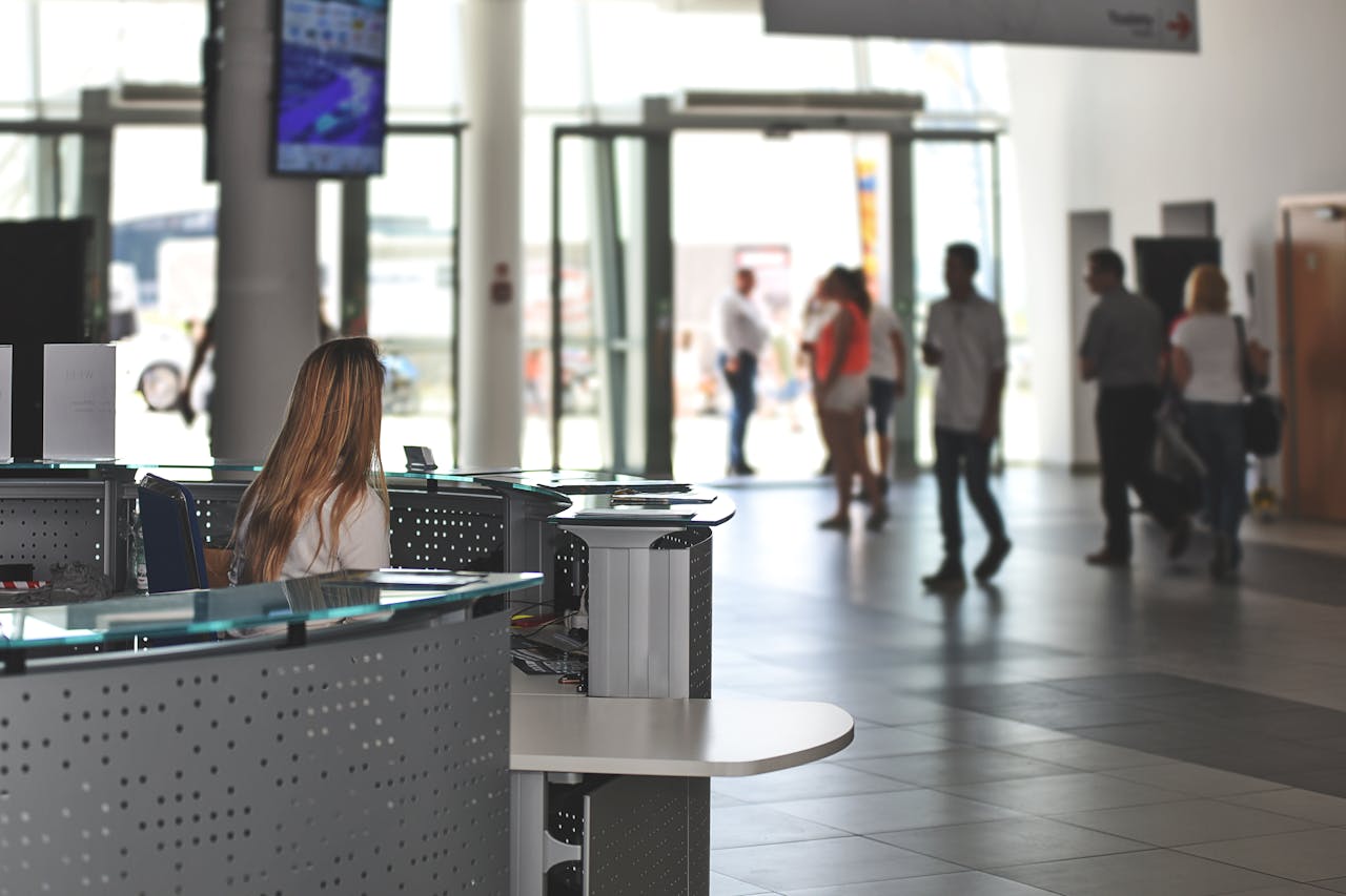 Modern office reception area with a receptionist at the front desk and people walking in the background.