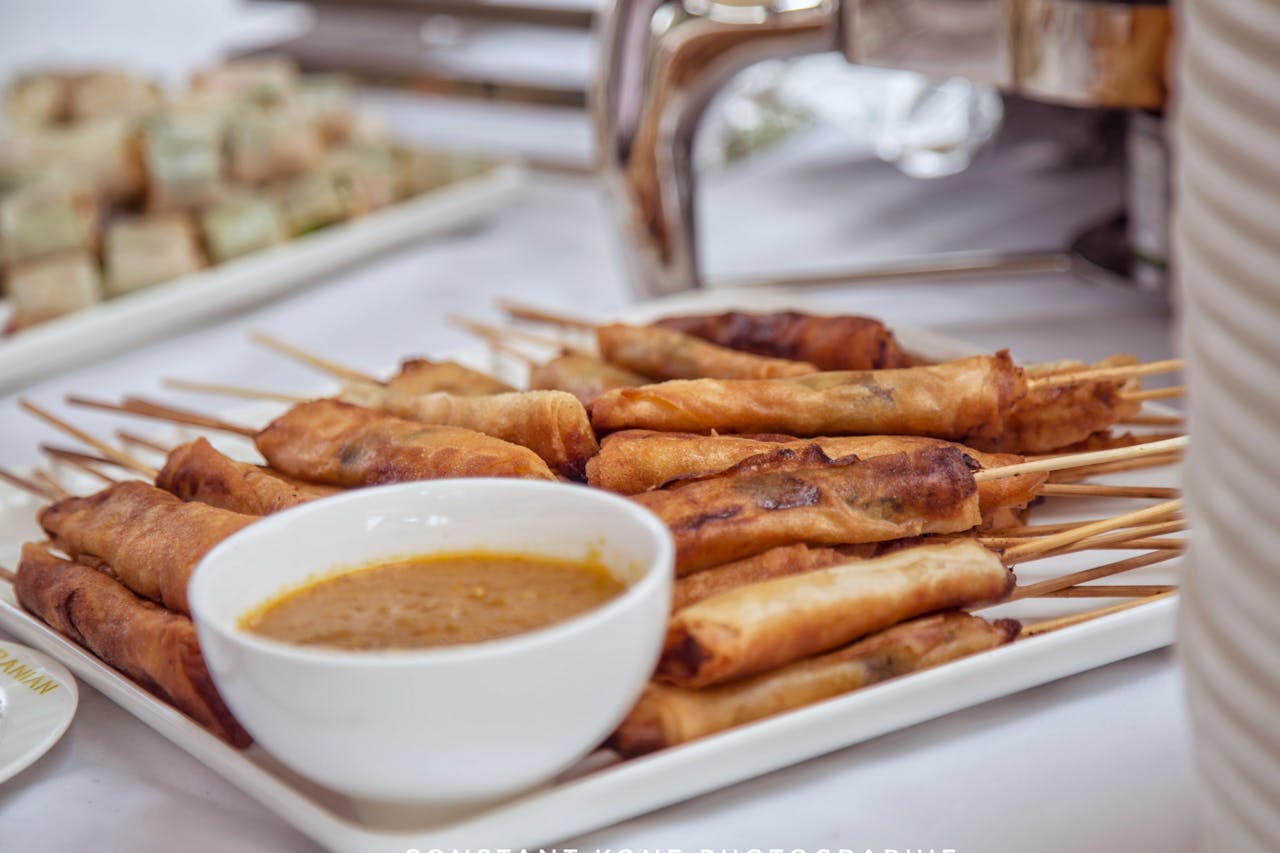 A platter of Filipino-style lumpia (spring rolls) on skewers, served with peanut sauce at a buffet event.
