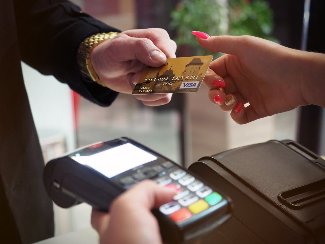 A person handing over a credit card for payment at a point-of-sale terminal, highlighting contactless transaction technology.