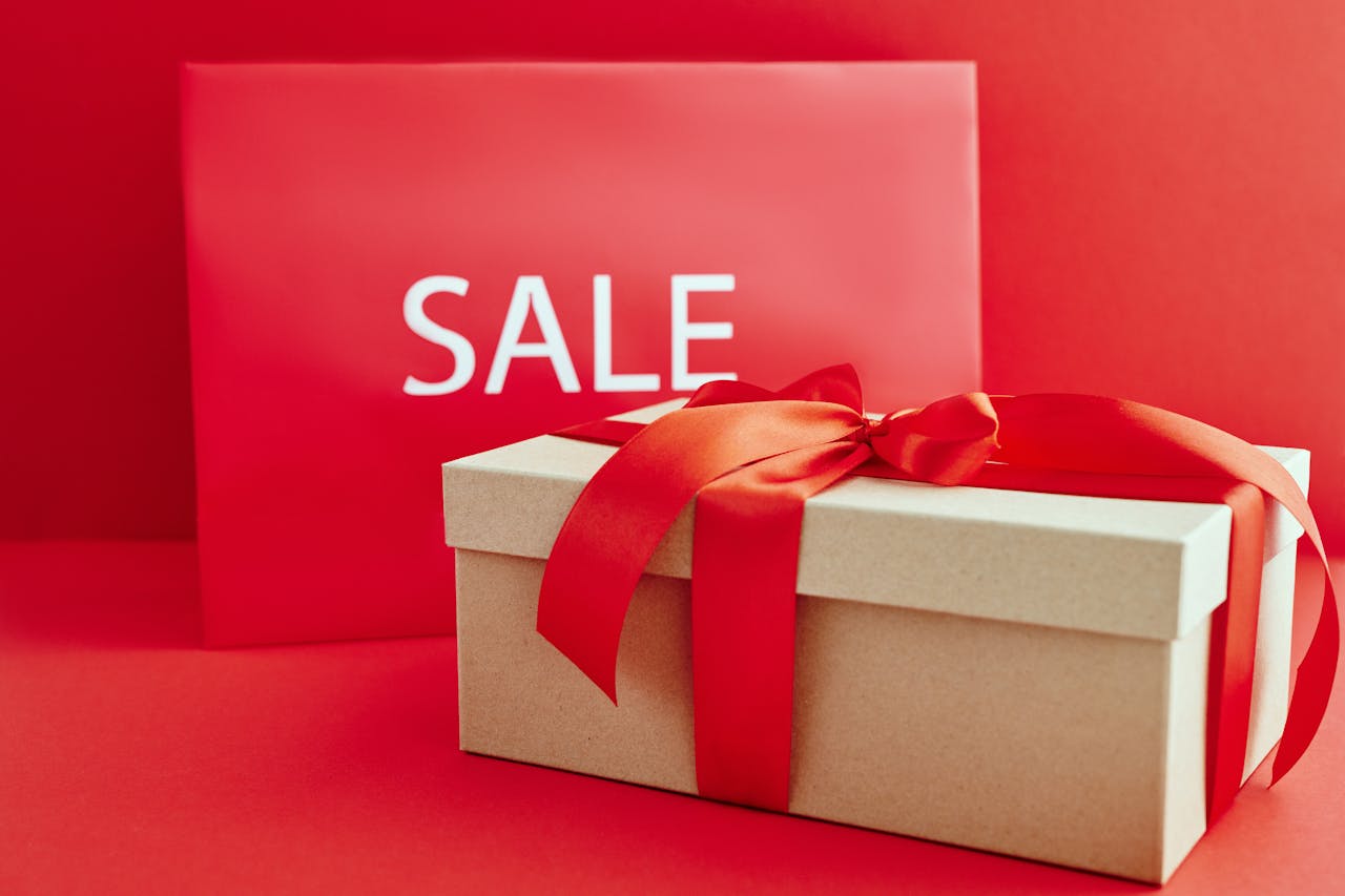 Gift box with red ribbon in front of a red SALE sign for holiday promotions