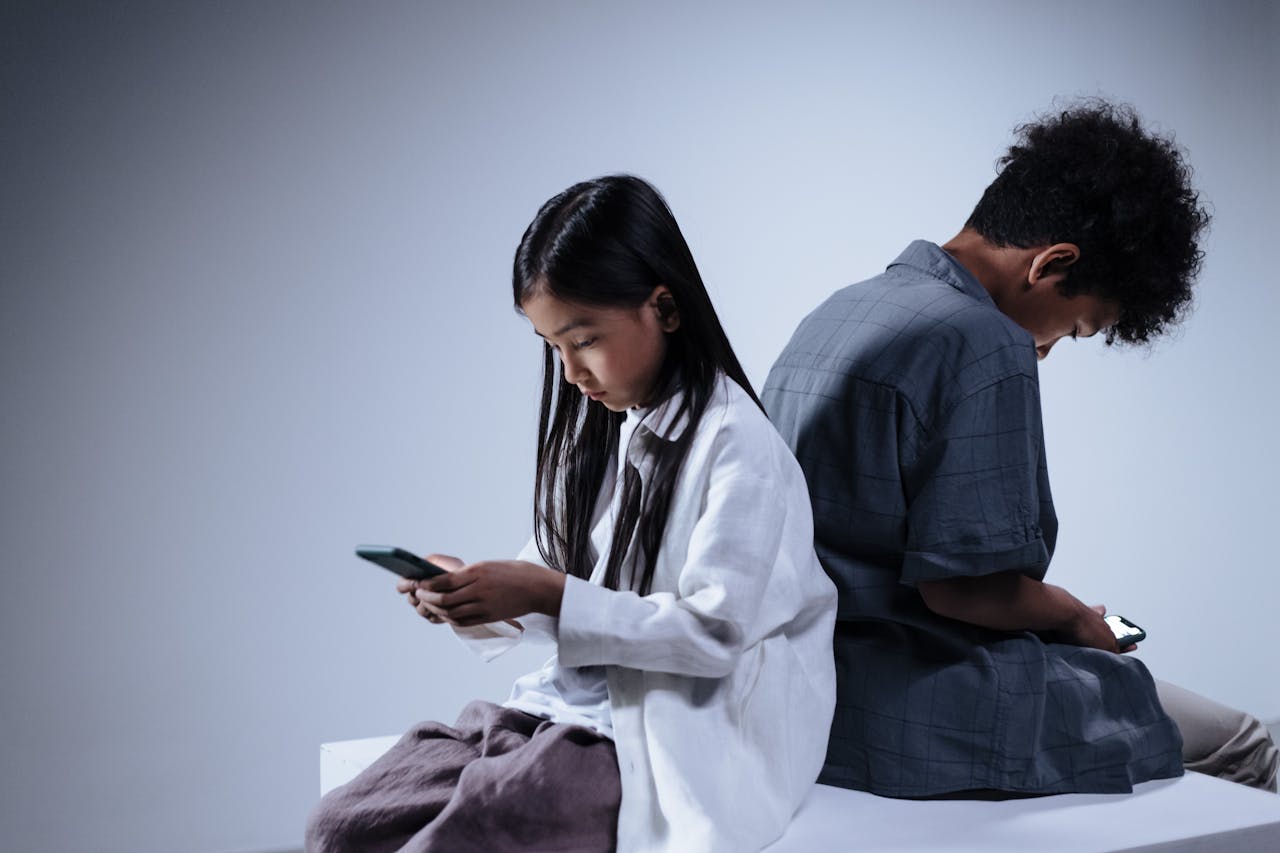 Two kids sitting back-to-back while using smartphones, highlighting screen time and digital habits among children