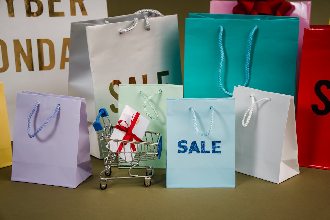 Colorful shopping bags with “SALE” signs and a gift in a mini shopping cart during Cyber Monday sale.
