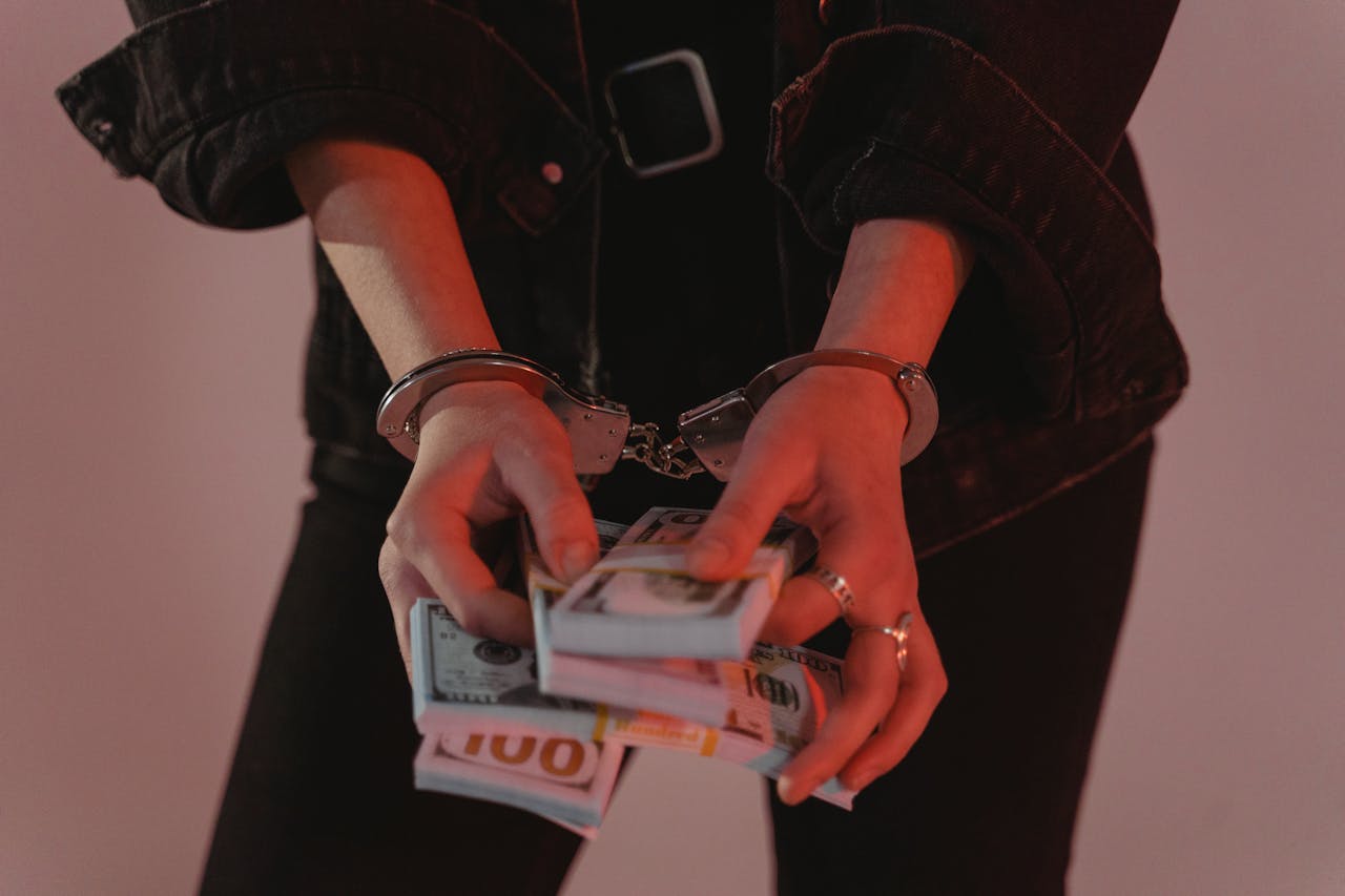Individual in handcuffs holding bundles of hundred dollar bills, symbolizing financial crime or fraud